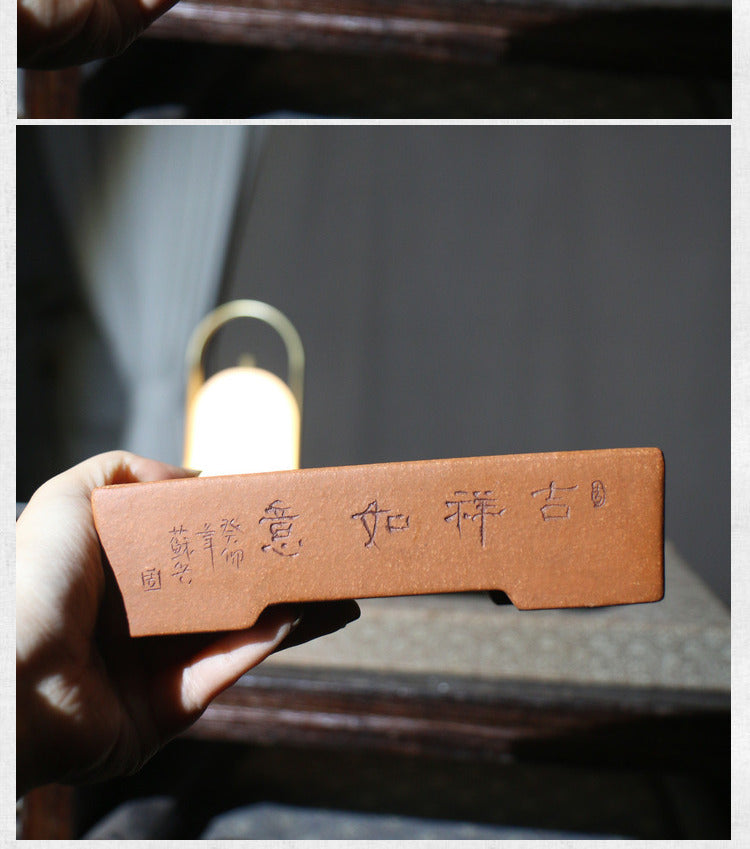 Hand holding the red-brown pot with calligraphy facing forward