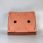 Underside of orange-brown rectangular pot showing two large openings and four small holes
