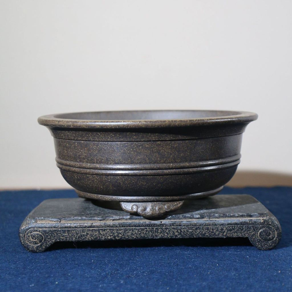 Dark round pot on a stone stand showing its banded walls