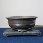 Dark round pot on a stone stand showing its banded walls