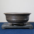 Front view of the dark pot on its stone stand