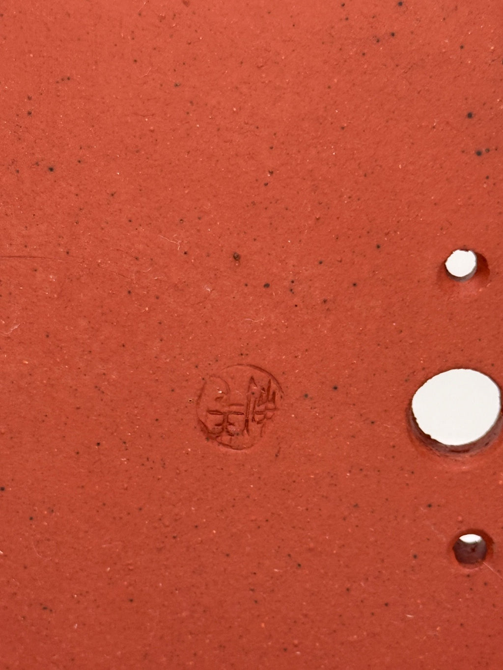 Close-up of an impressed circular seal and drainage openings in the red pot's base
