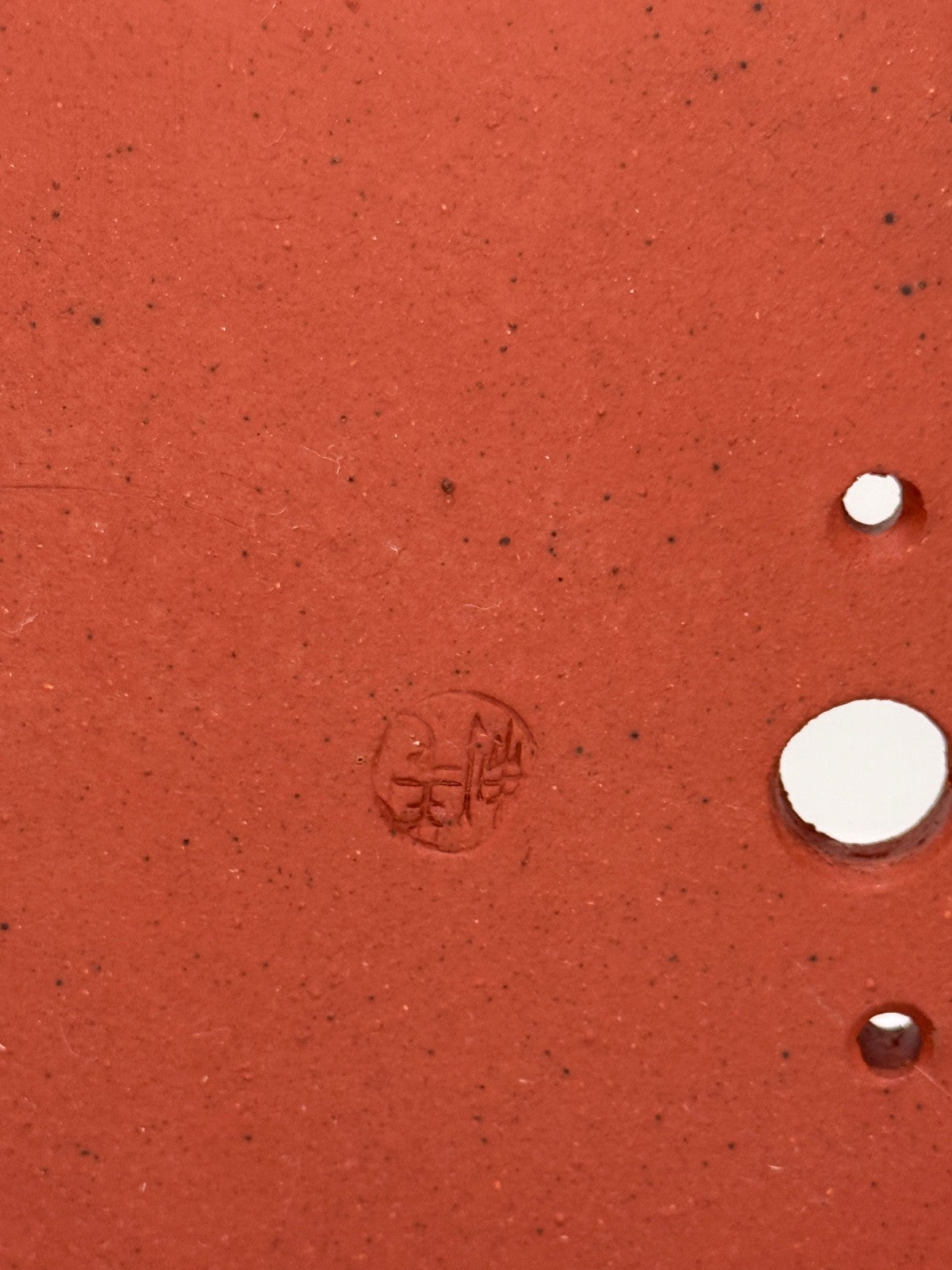 Close-up of an impressed circular seal and drainage openings in the red pot's base