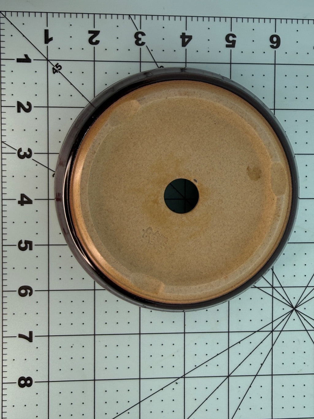 Underside of the round pot showing a pale base and one central drainage hole