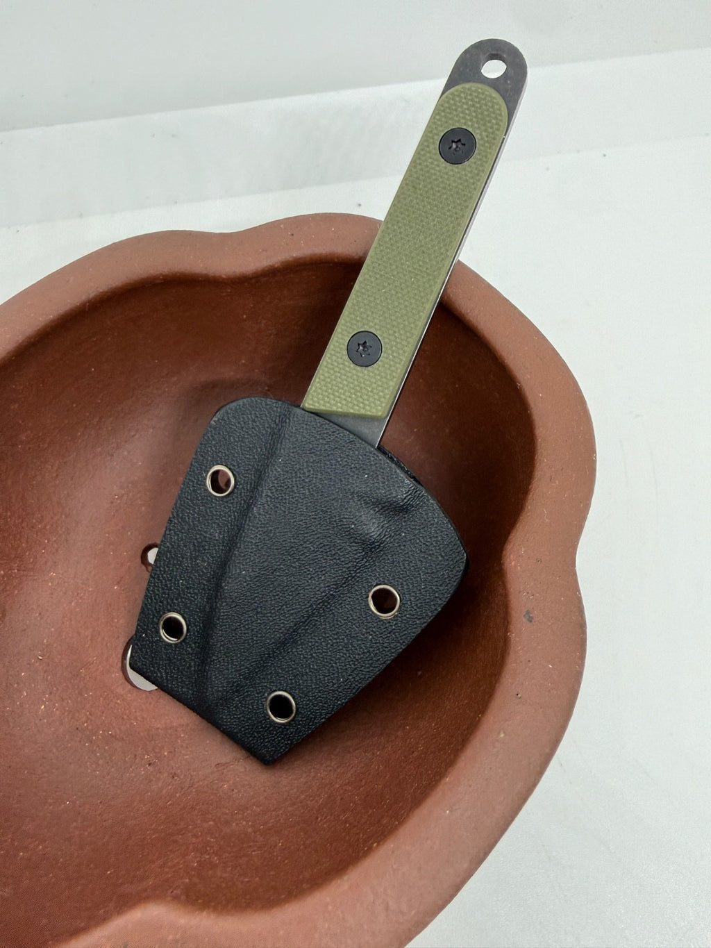 Olive-handled knife in a black fitted sheath resting inside a brown pot
