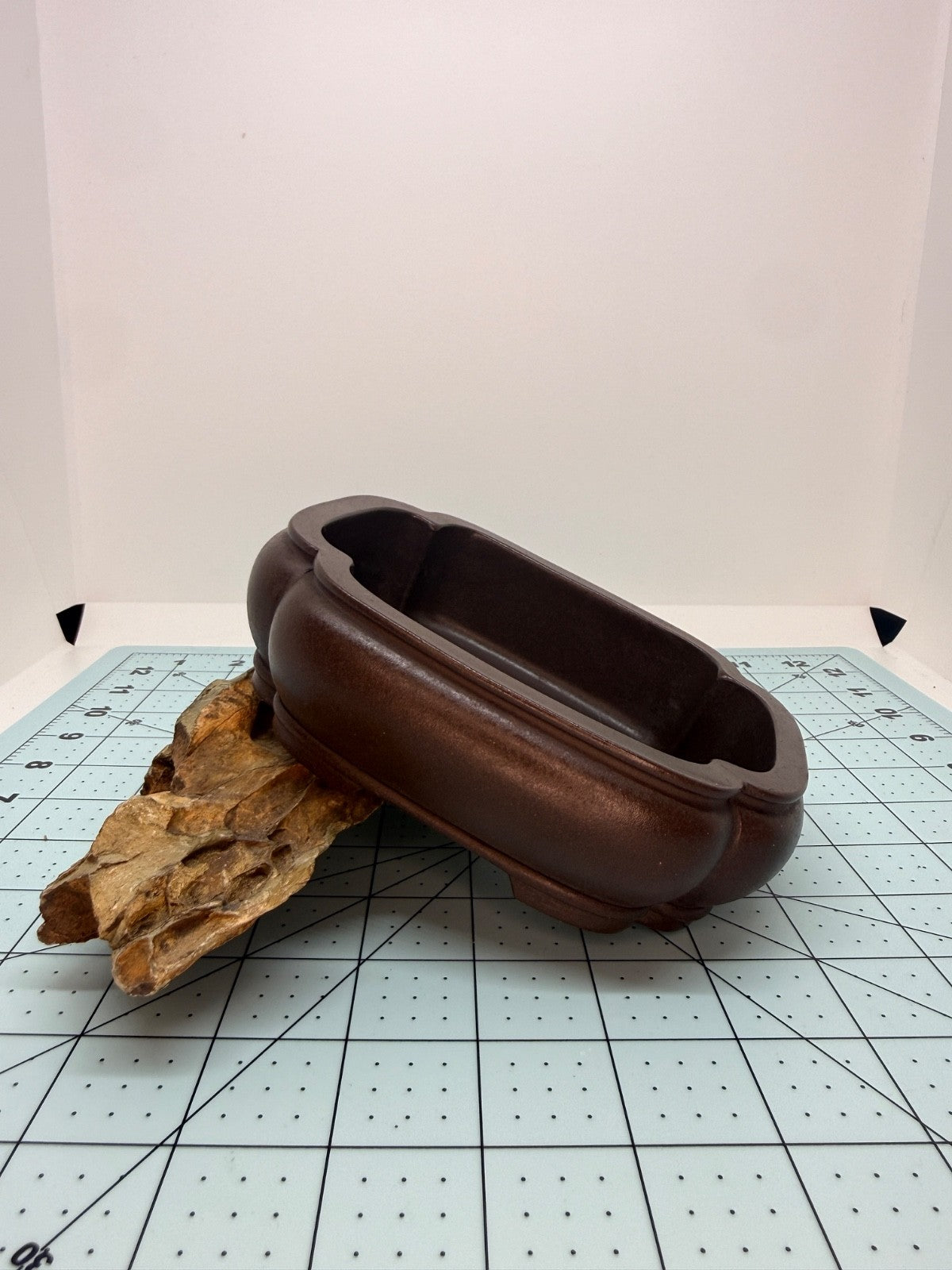 Brown mokko bonsai pot tilted on a rock to show its rounded side and layered rim