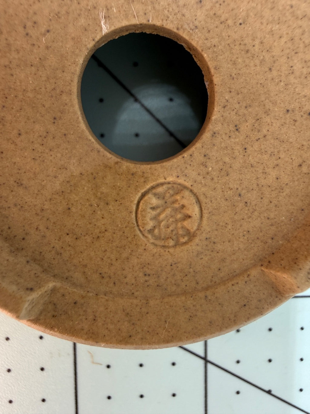 Close-up of the ochre pot's impressed circular seal and central drainage hole