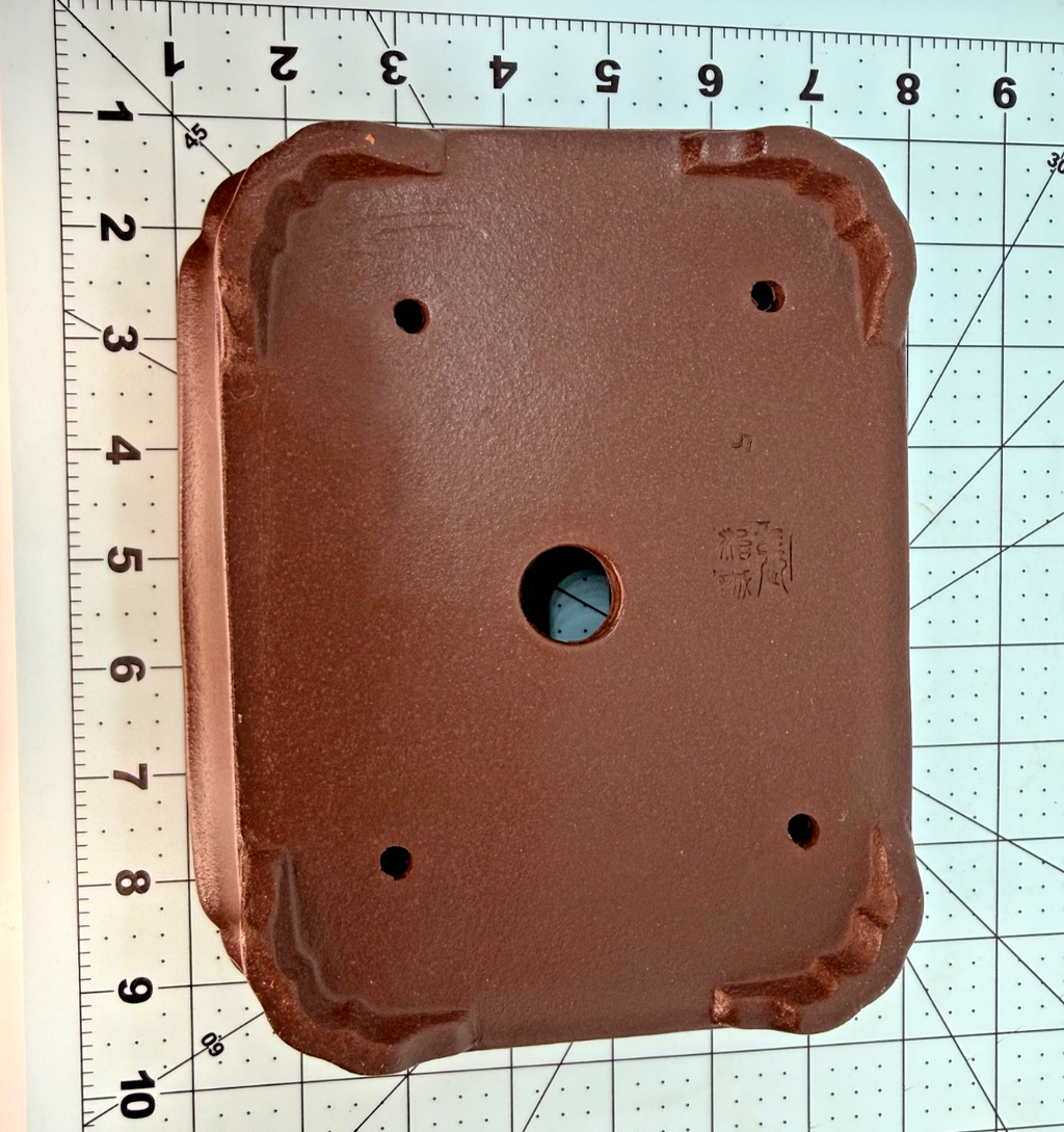 Underside of the brown rectangular pot with one central drainage hole, four smaller openings and shaped feet