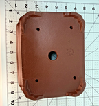 Underside of the brown rectangular pot with one central drainage hole, four smaller openings and shaped feet