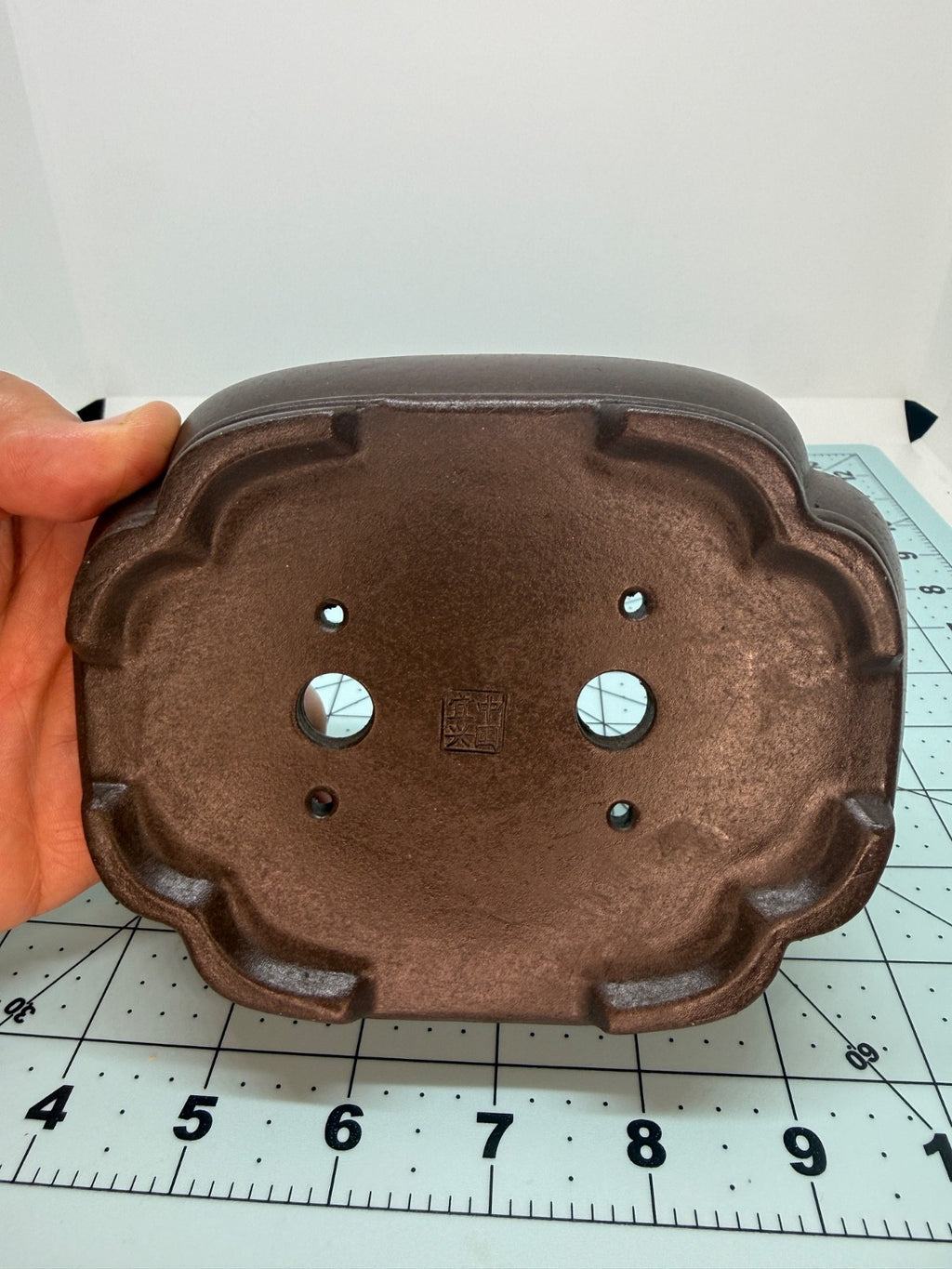 Hand-held underside view of the brown mokko pot with two drainage holes and four smaller openings