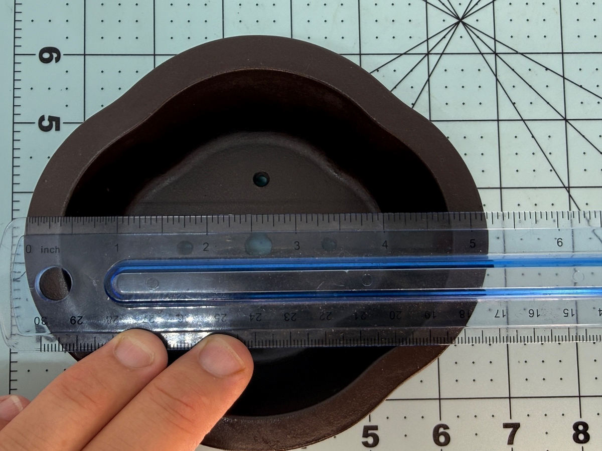 Ruler across the length of the brown oval pot's lobed interior opening