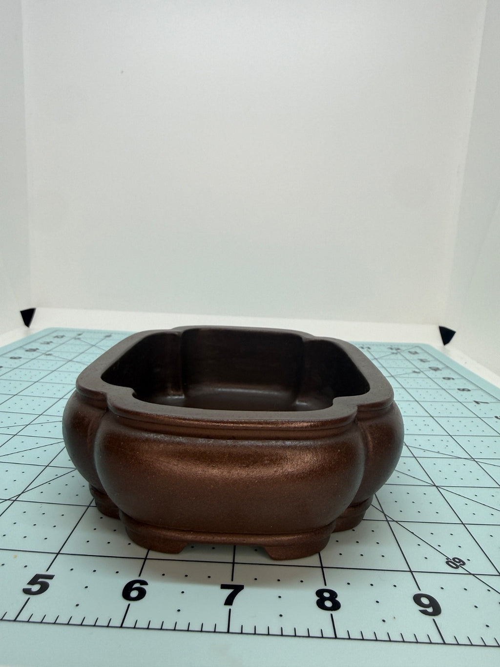 Short-side view of the brown lobed bonsai pot on a gridded measuring mat