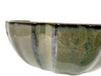 Close-up of the green-gray pot's curved fluted wall and dark glaze streaks