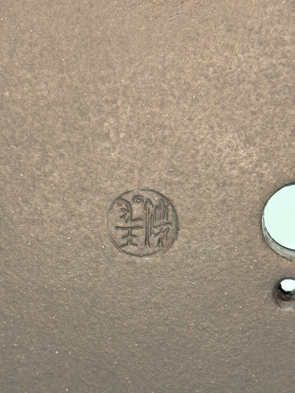 Close-up of an impressed circular seal beside drainage openings in the brown clay base