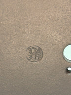 Close-up of an impressed circular seal beside drainage openings in the brown clay base