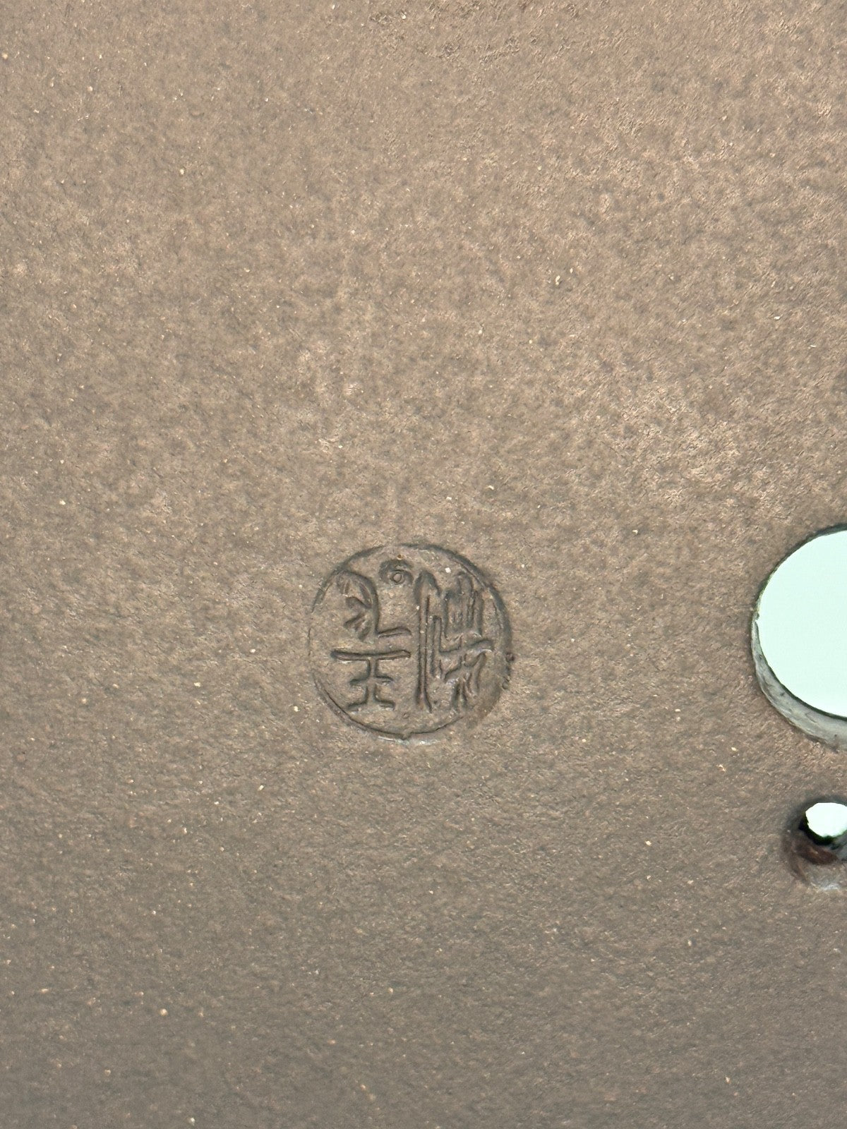 Close-up of an impressed circular seal beside drainage openings in the brown clay base