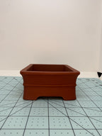Short-side view of the red pot showing its flared rim and cutout between the feet