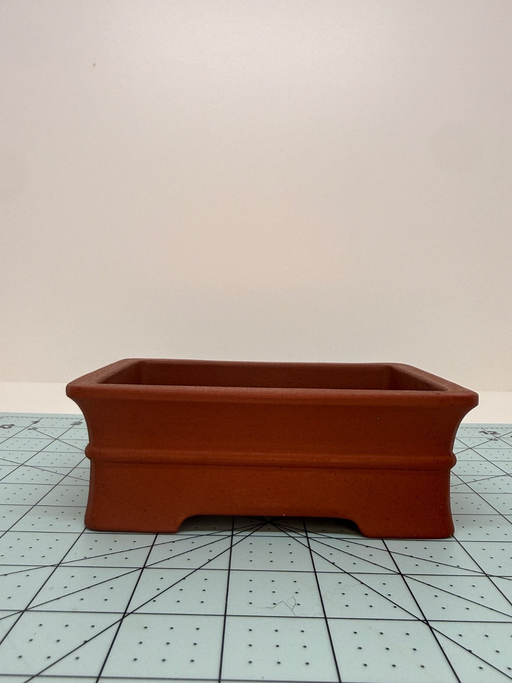 Long-side view of the red rectangular pot on a gridded measuring mat