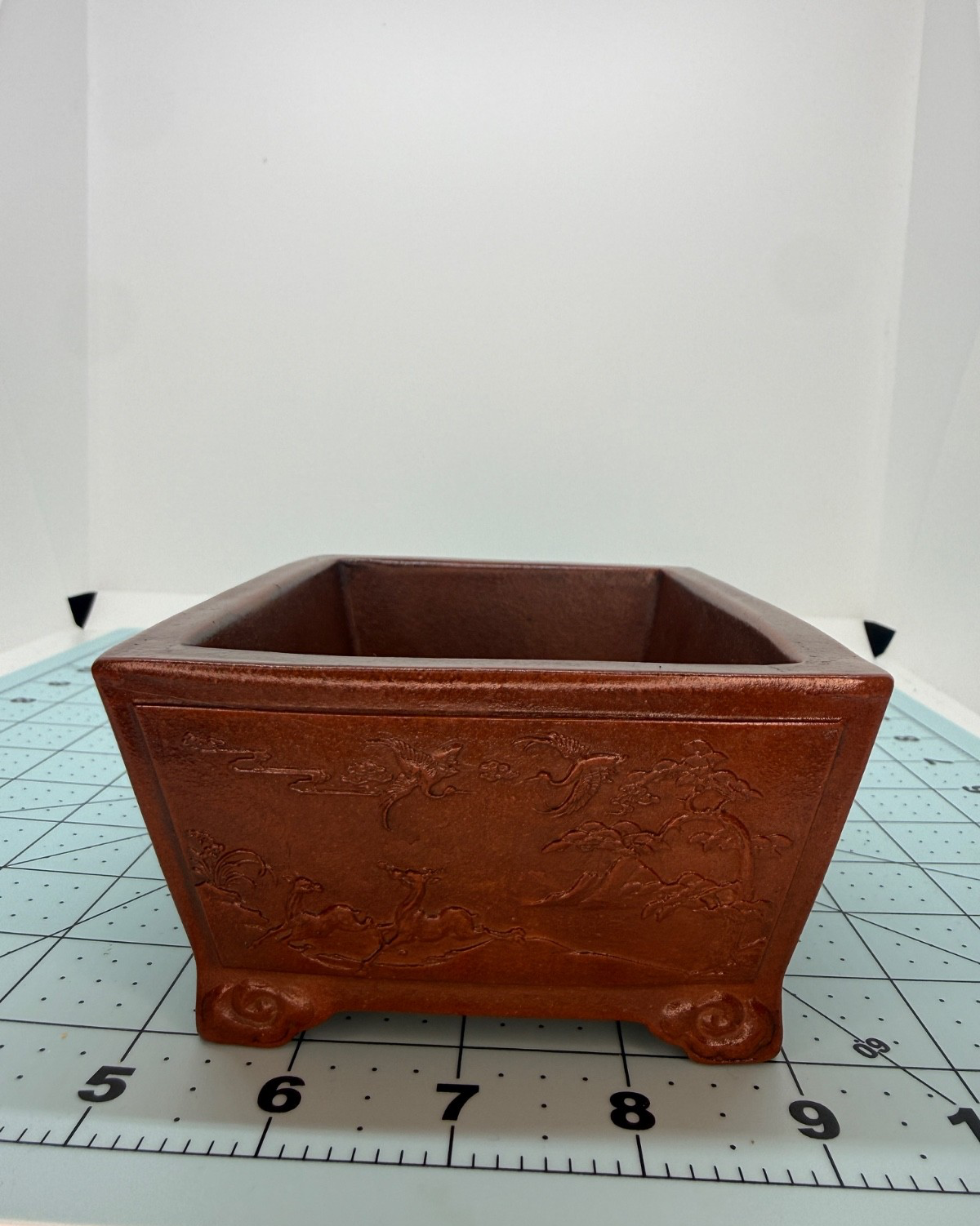 Short-side view of the reddish-brown pot showing relief decoration and curled feet