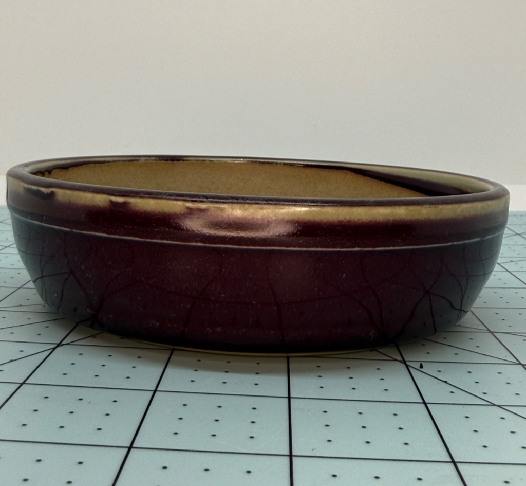 Angled side view of the plum-glazed round pot showing crackle lines