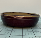 Angled side view of the plum-glazed round pot showing crackle lines