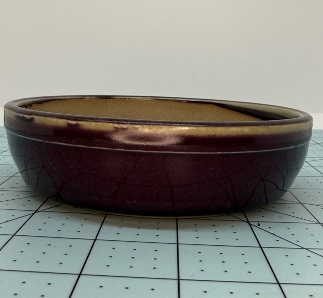 Angled side view of the plum-glazed round pot showing crackle lines