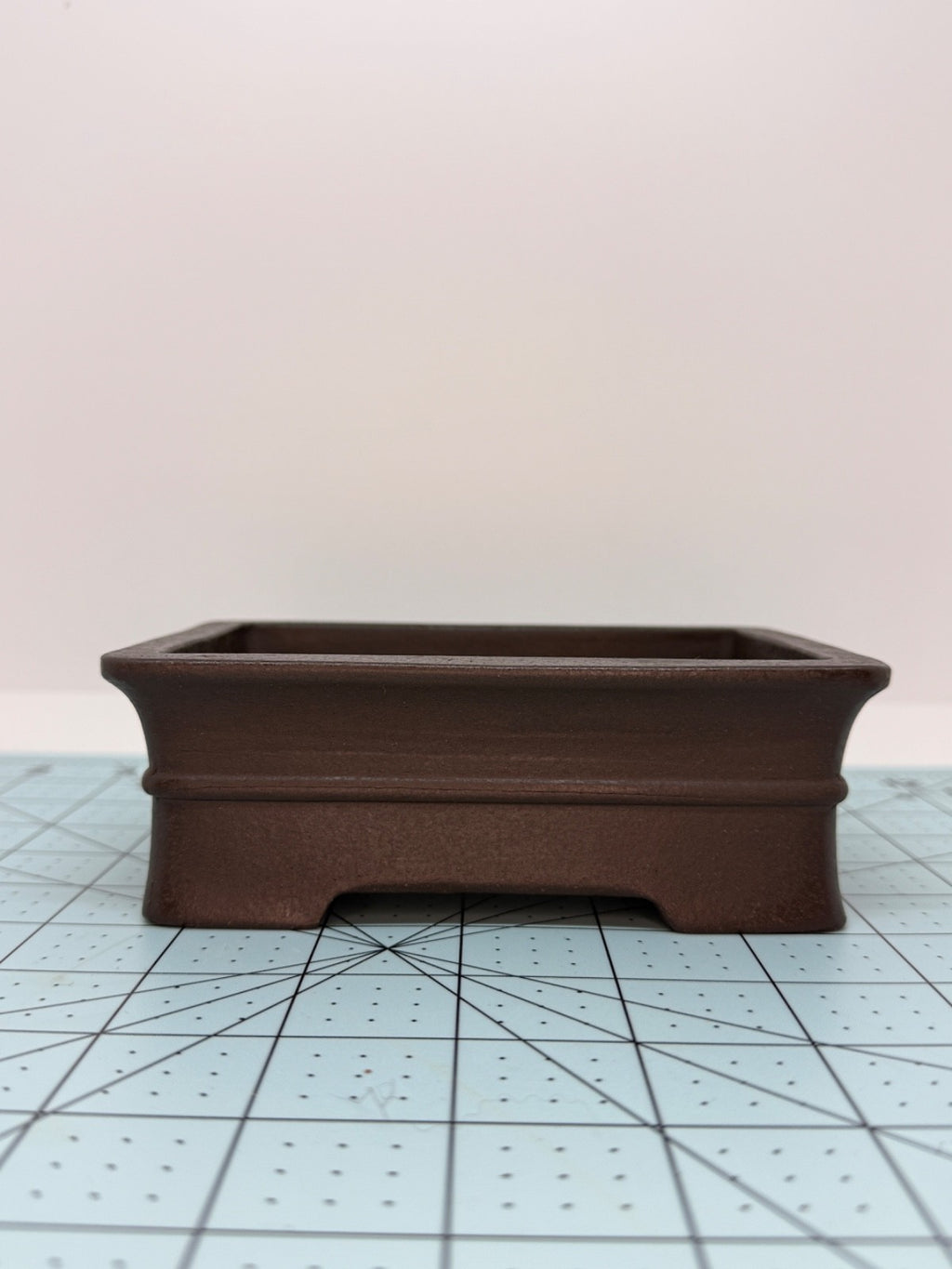 Low front view of the dark brown pot showing its horizontal band and foot cutout