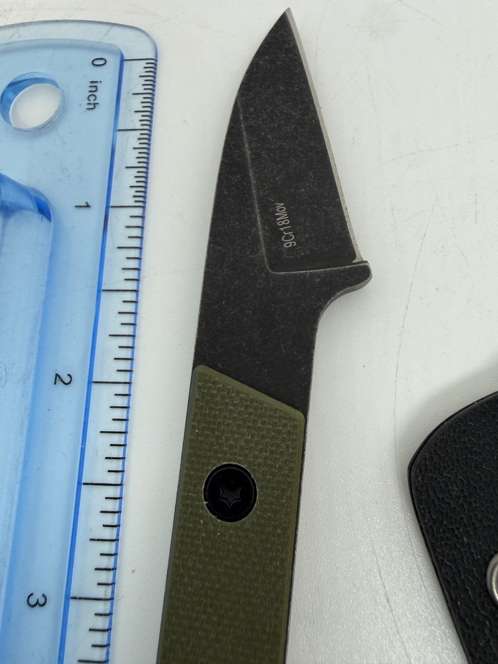 Unsheathed pointed dark knife blade and olive handle beside a ruler