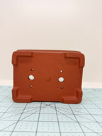 Underside of the red rectangular pot showing corner feet, two drainage holes and four smaller openings