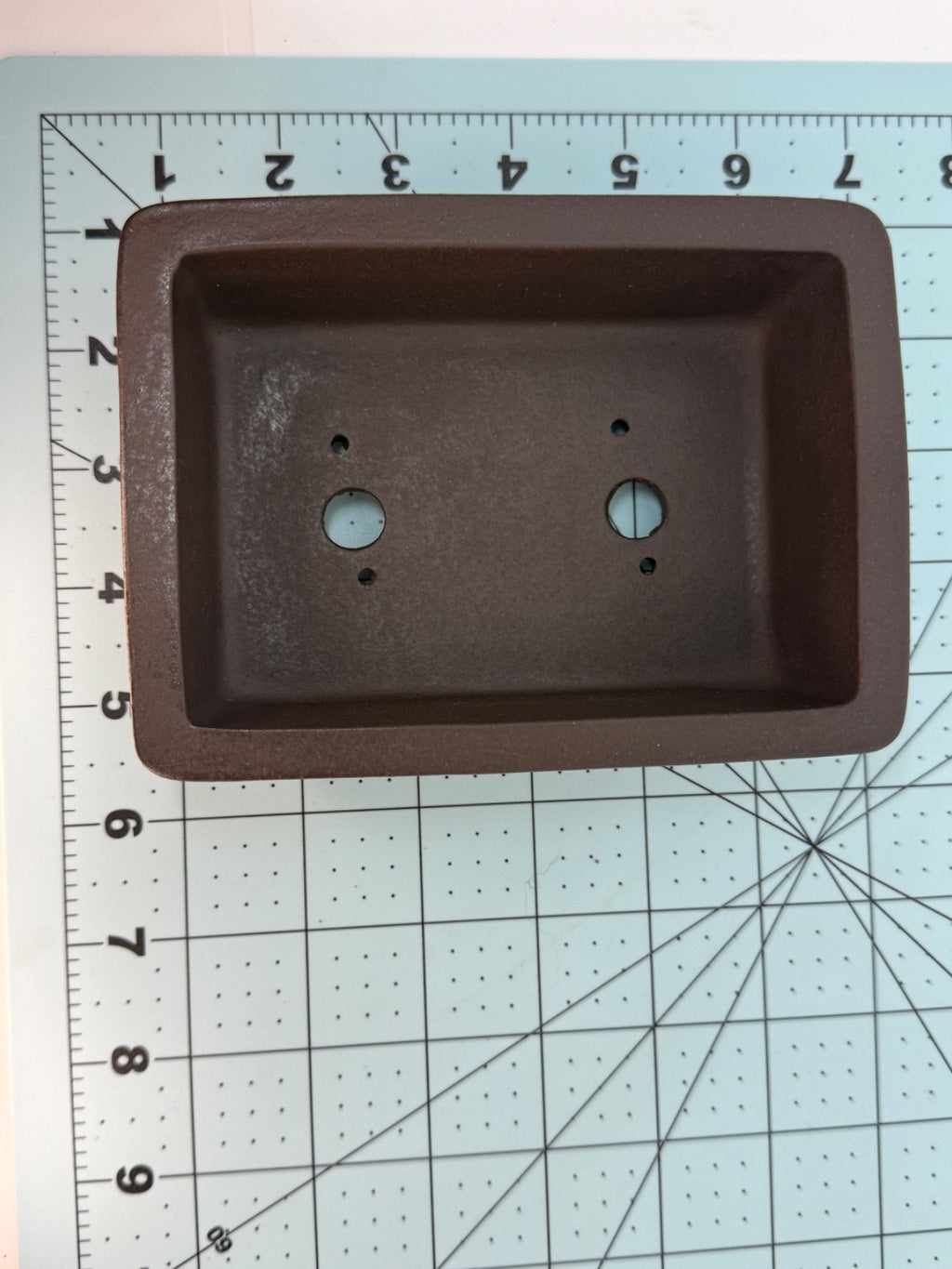 Top view of the dark brown rectangular pot on a measuring mat, showing two drainage holes