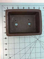 Top view of the dark brown rectangular pot on a measuring mat, showing two drainage holes