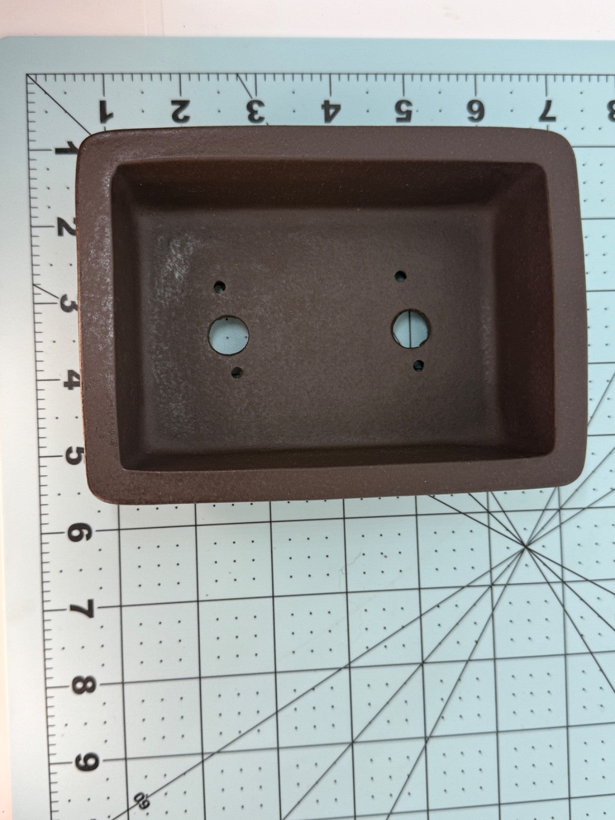 Top view of the dark brown rectangular pot on a measuring mat, showing two drainage holes