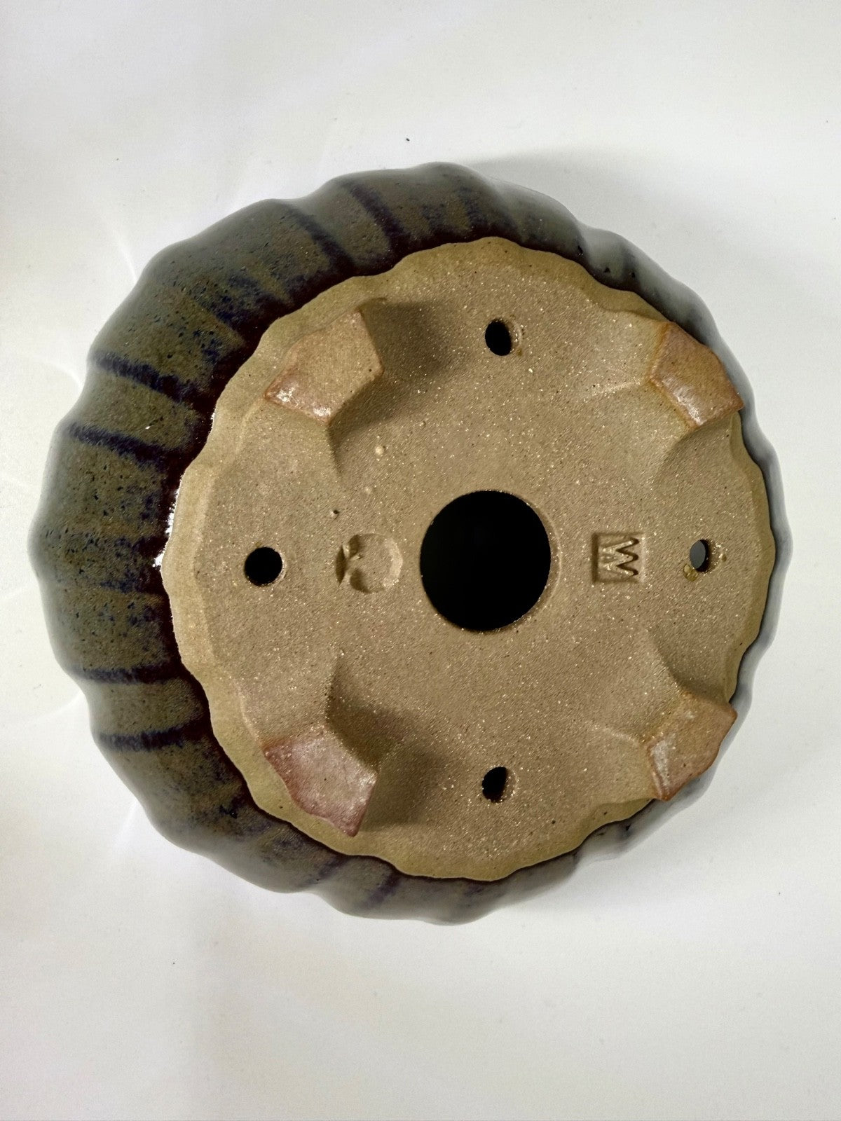 Underside of the green-gray pot showing feet, drainage openings and impressed marks