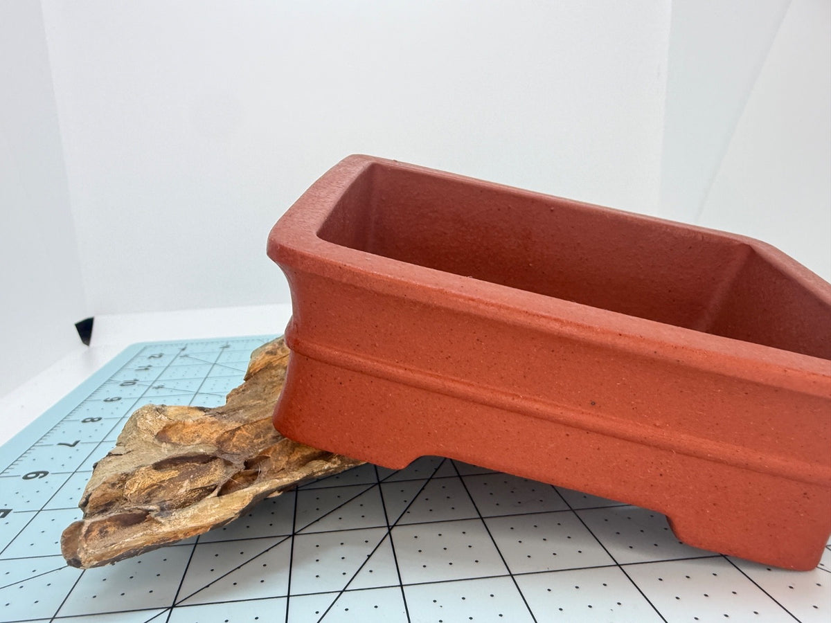 Red rectangular bonsai pot tilted on a rock to show its side wall and rim