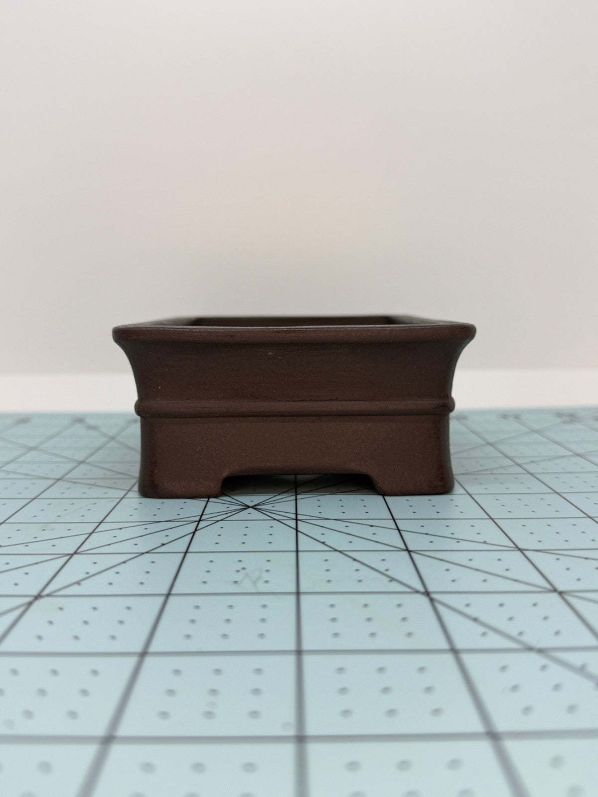 Short-side view of the dark brown rectangular pot on a gridded mat