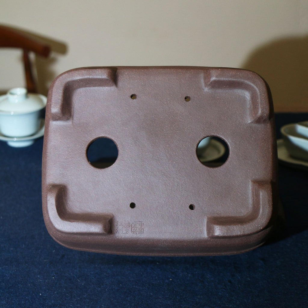 Underside of purple-brown rectangular pot showing openings and corner feet