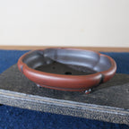 Angled view of lobed red-brown bonsai pot showing dark interior