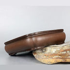 Brown shallow rectangular pot tilted on a rock to show its rounded side