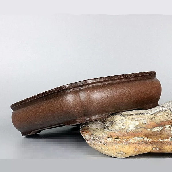 Brown shallow rectangular pot tilted on a rock to show its rounded side