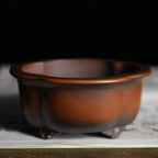 Amber-brown lobed bonsai pot with dark base and decorative feet
