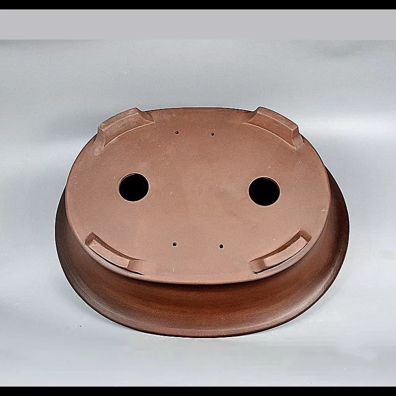 Underside of brown oval pot showing two large openings and feet