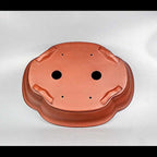Underside of red-orange lobed pot showing openings and sculpted feet