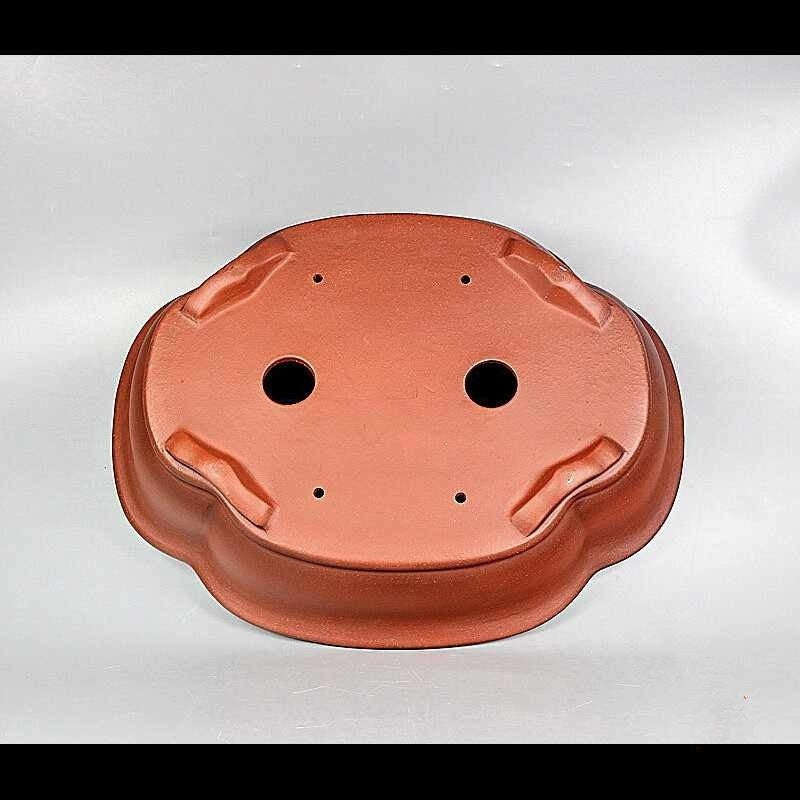 Underside of red-orange lobed pot showing openings and sculpted feet