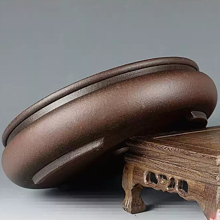 Rounded brown pot tilted on a carved wooden stand