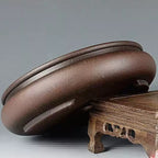 Rounded brown pot tilted on a carved wooden stand