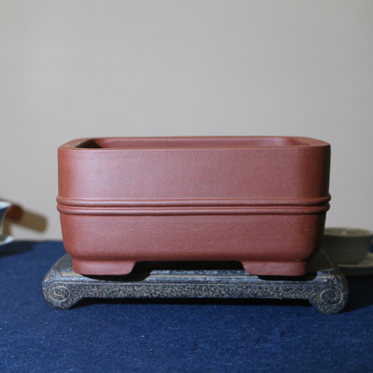Red-brown rounded rectangular pot with double band on a stone stand