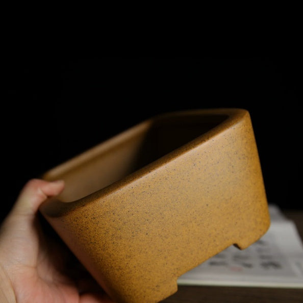 Hand-held side view showing the ochre pot's speckled glaze and rounded corner
