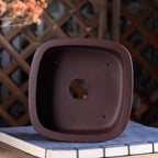 Top view of brown rounded square pot showing central opening and four small holes