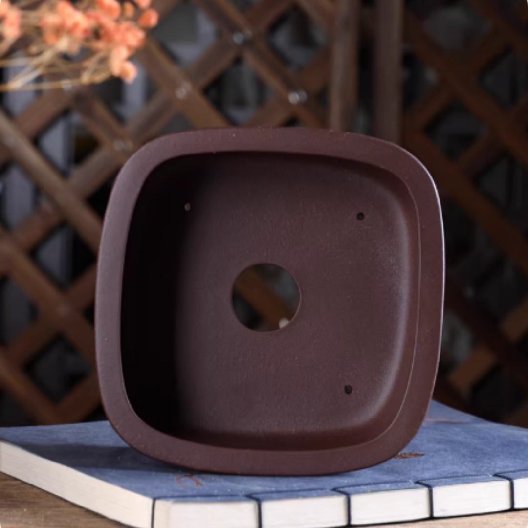 Top view of brown rounded square pot showing central opening and four small holes