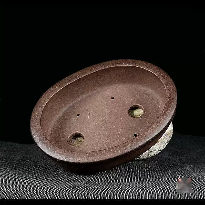 Brown oval pot tilted to show two drainage holes in its interior